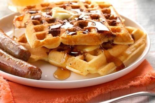 a plate of waffles with syrup and a sausage at Rosemont B&B Cottages in Little Rock