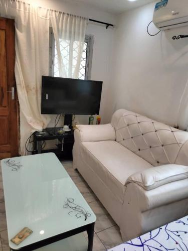 a living room with a white couch and a table at Studio moderne où tout est Neuf, Cuisine, Couvert,ClimatiséWifi haut débit , Smart TV à bertoua in Bertoua