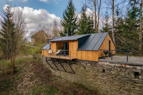 a wooden cabin with a black roof on a stone wall at Chalet Nebeská v Orlických horách in Rokytnice v Orlických Horách