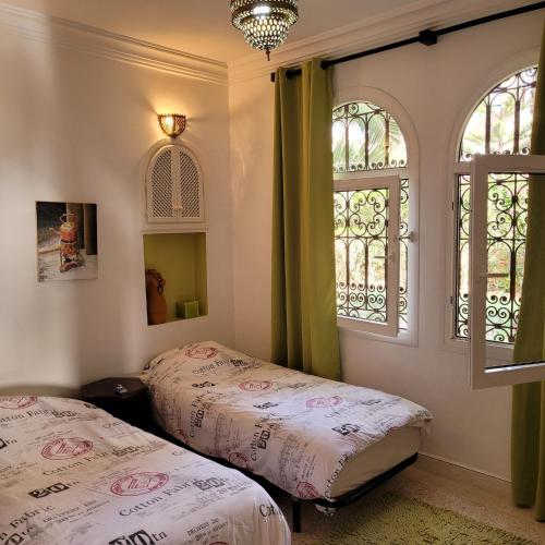 a bedroom with two beds and two windows at Villa du soleil in Mirleft