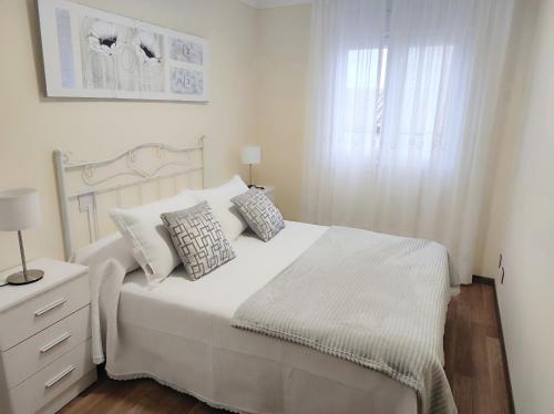 a white bedroom with a white bed and a window at O AREAL DE NATALIA in Muxia