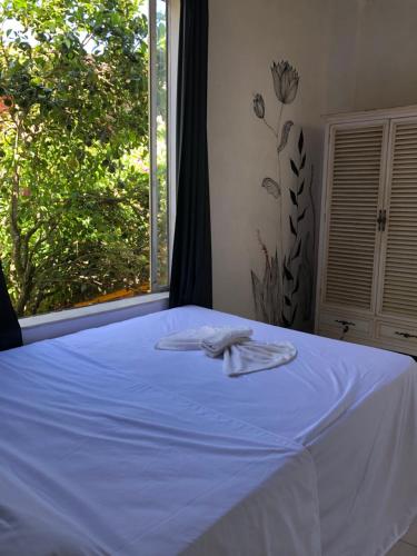 a bed with a white sheet and a window at Banana Leaf Eco Hostel in Barra de Guaratiba