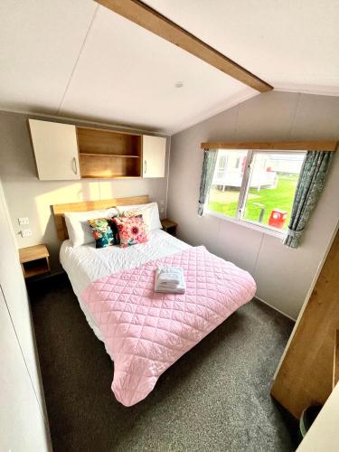 a small bedroom with a pink bed and a window at KEE Holiday Home Caravan in Great Yarmouth