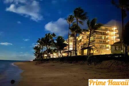 a hotel on a beach with palm trees at night at Amazing 7th floor Beachfront Condo in Hauula