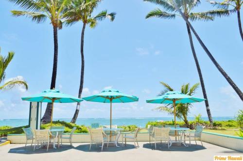a patio with tables and chairs and palm trees at Amazing 7th floor Beachfront Condo in Hauula