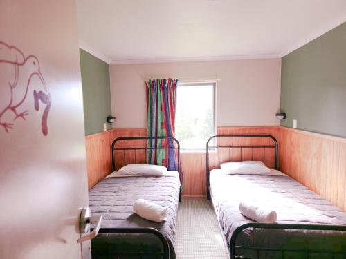 two beds in a small room with a window at Waitomo Village Chalets home of Kiwipaka in Waitomo Caves