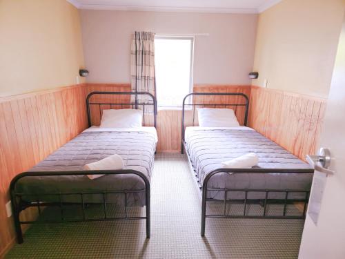 two beds in a small room with a window at Waitomo Village Chalets home of Kiwipaka in Waitomo Caves