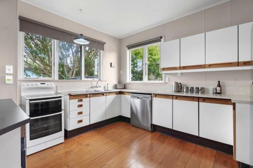 a kitchen with white cabinets and wooden floors and windows at Charming 3 Bedroom Family Home Pet Friendly in Hamilton