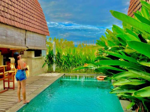 a woman standing next to a swimming pool next to a house at Bhumi Lovina Residence & Villa in Singaraja