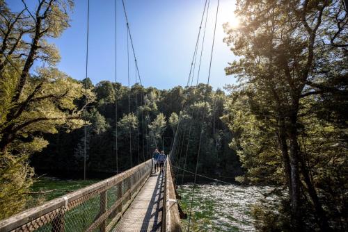 two people walking across a suspension bridge over a river at Tasman Holiday Parks - Te Anau in Te Anau