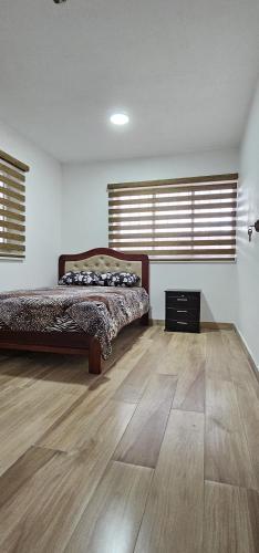 a bedroom with a bed and wooden floors and windows at La Frontera Departamento in Tulcán