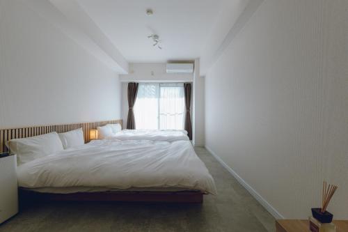 a bedroom with a bed with white sheets and a window at Coda House in Aoichō