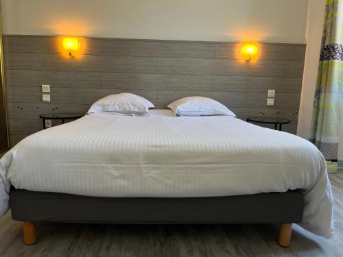 a large white bed with two pillows on it at Hôtel Le Lacuzon in Moirans-en-Montagne