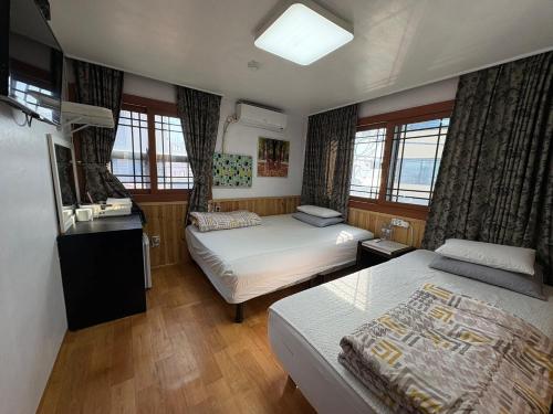 a bedroom with two beds and a television and windows at Gudeok Guesthouse in Seogwipo