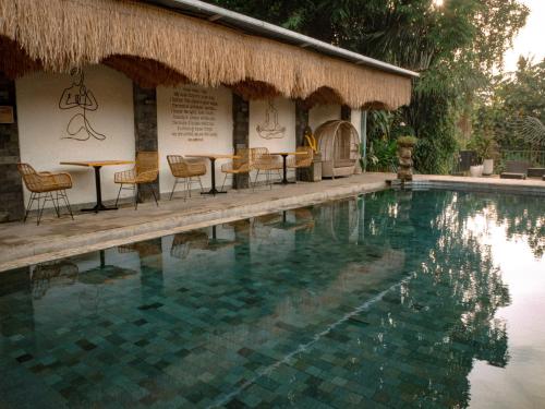 a swimming pool with chairs and a table and a building at Tattva Ubud Retreat & Wellness in Ubud