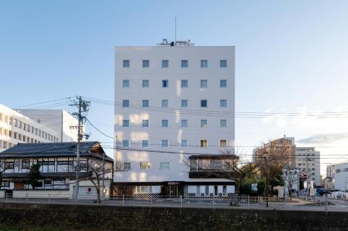 a tall white building in a city with buildings at Hotel Matsumoto Yorozuya in Matsumoto