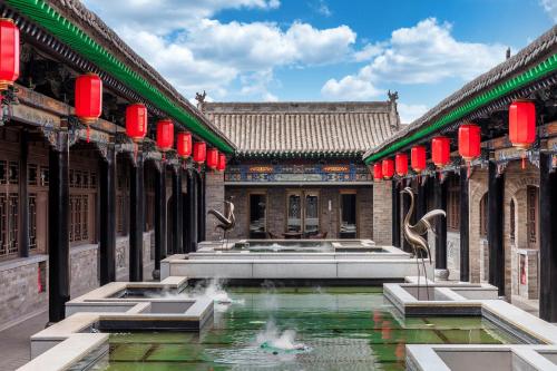 a courtyard with a fountain in a building with red lanterns at Xinghuacun Hotel in Pingyao