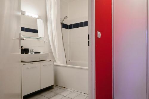 La salle de bains est pourvue d'un lavabo blanc, d'une baignoire et d'une porte rouge. dans l'établissement Élégant appartement avec balcon privé à Lille, à Lille