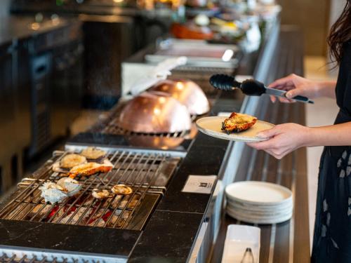 a woman holding a plate of food on a grill at FIVE SPRING RESORT THE SHIRAHAMA in Shirahama
