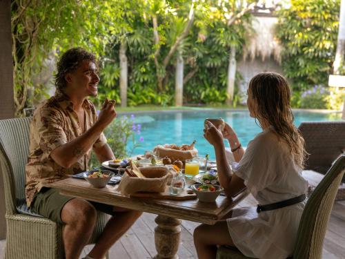 a man and a woman sitting at a table eating food at Blue Karma Dijiwa Seminyak in Seminyak