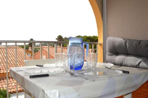 une table avec des verres et un vase bleu sur un balcon dans l'établissement NP170-A240 Appartement 2 pièces Narbonne Plage, à Narbonne-Plage