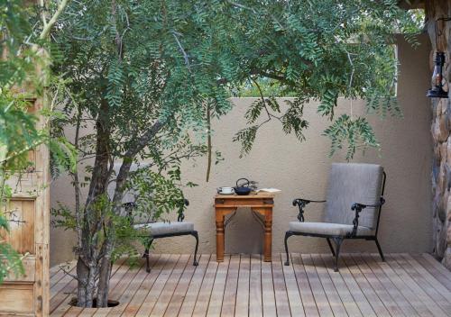 two chairs and a table on a patio with trees at Geiger's Camp in Timbavati Game Reserve by NEWMARK in Timbavati Game Reserve