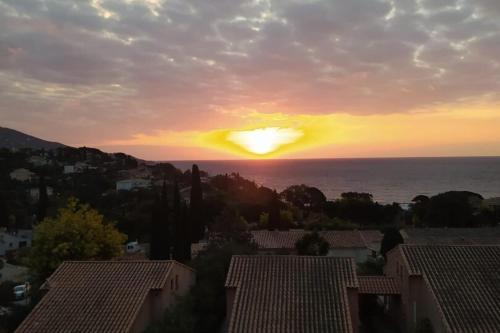 un coucher de soleil sur l'océan avec des maisons et des toits dans l'établissement Duplex in Pramousquier - sea view, au Lavandou