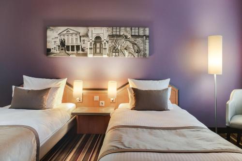 two beds in a hotel room with a painting on the wall at Leonardo Hotel Weimar in Weimar