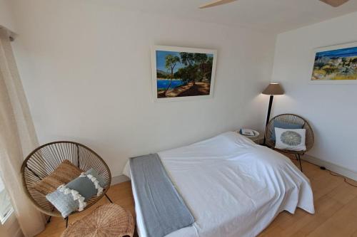 - une chambre avec un lit et deux chaises en osier dans l'établissement T2 vue à 100m de la plage avec parking privé, à Bormes-les-Mimosas
