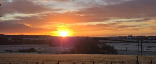 a sunset with the sun setting over a field at Stonehenge Shepherds Huts in Durrington