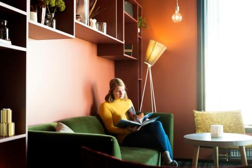 a woman sitting in a green chair reading a book at Svalbard Hotell | The Vault in Longyearbyen