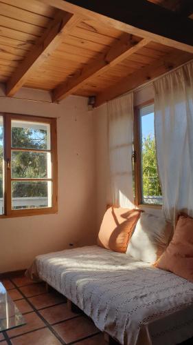 una cama en una habitación con dos ventanas en Simpática y Funcional Cabaña en San Martín, en San Martín de los Andes