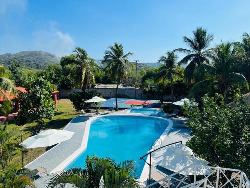 a large swimming pool with umbrellas and palm trees at Villa Rosa Bella Perfect for families or groups in Palmar de Ocoa