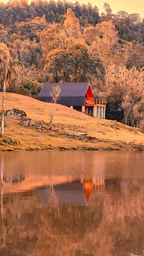 a red barn sitting on a hill next to a lake at Cabana Água - Cabanas Recanto do Lago in Nova Petrópolis