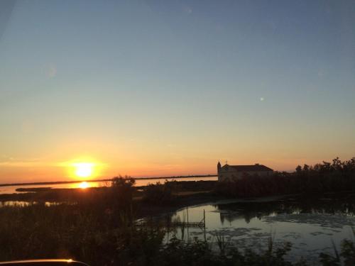 a sunset over the water with a house in the distance at La Casina del Delta del Po in Porto Viro