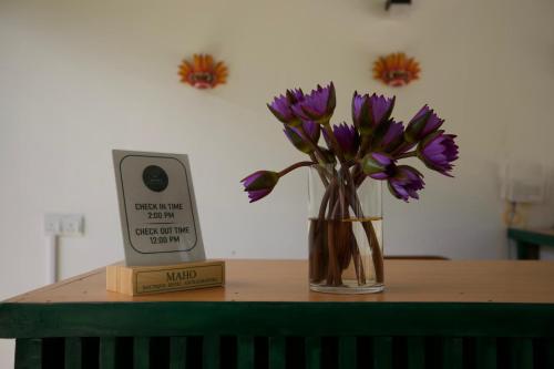 a table with a vase with purple flowers and a clock at Maho Boutique Hotel in Anuradhapura