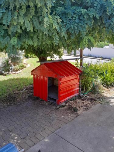 a red dog house sitting under a tree at Red Kennel Budget Private Rooms - Trott Park in Happy Valley