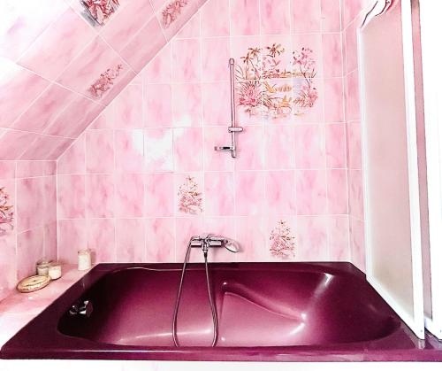 La salle de bains est pourvue d'une baignoire violette et de carrelage rose. dans l'établissement Maison Familiale tout confort, à Mouen