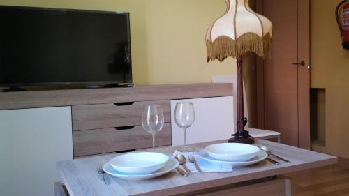 a table with two plates and glasses and a television at Apartamentos Turísticos La Garza in Cáceres