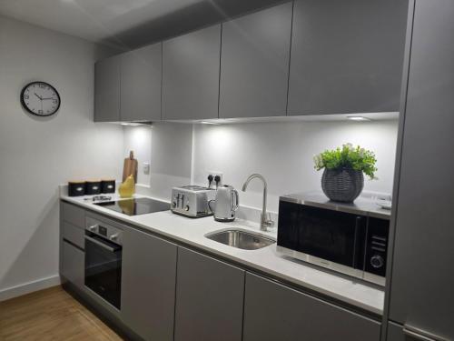 a kitchen with stainless steel appliances and a clock on the wall at Snuggle Inn Serviced Apartments, Great choice for large groups, Contractors, Business Executives and Family Vacations in the stunning valley of Surrey Hills, secure Private Parking, Offering Easy Train Access to London, Gatwick airport, M25 in Warlingham