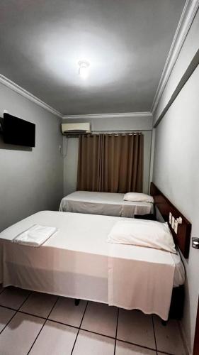 two beds in a small room with a tv at Serras Hotel in Rondonópolis