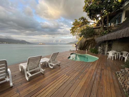 a deck with chairs and a swimming pool next to the water at Lindo Loft a beira Mar em Ilha Bela Acesso ao mar in Ilhabela
