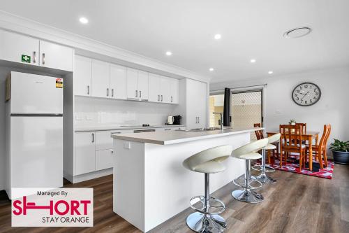 a kitchen with white cabinets and a counter with stools at Wolaroi Villa 1, with Netflix and Disney Plus in Orange