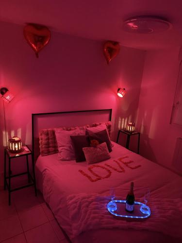 une chambre rose avec un lit avec une bouteille de vin dessus dans l'établissement Suite Eden Spa, Appart'hôtel bien être , Patio de standing barbecue - TV XL CinéSport, Lit Q-Size, Wifi, P-Gratuit en Résidence, à Avion