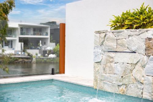 a swimming pool with a stone wall next to a house at Stylish 4-Bed Waterfront Home with Private Pool in Maroochydore