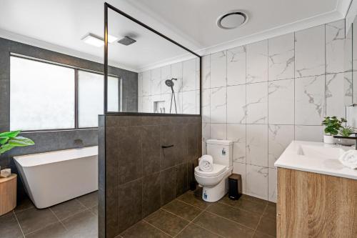 a bathroom with a tub and a toilet and a sink at Newcastle Escape 4-Bedroom House in Hamilton