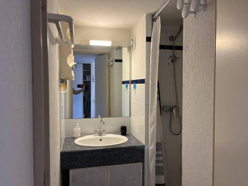 La salle de bains est pourvue d'un lavabo et d'une personne dans le miroir. dans l'établissement T3 climatisé avec parking et piscine à 200m de la plage au Cap d'Agde - FR-1-749-75, au Cap d'Agde