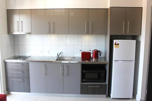 a kitchen with gray cabinets and a white refrigerator at CDU Village Casuarina Campus in Jingili