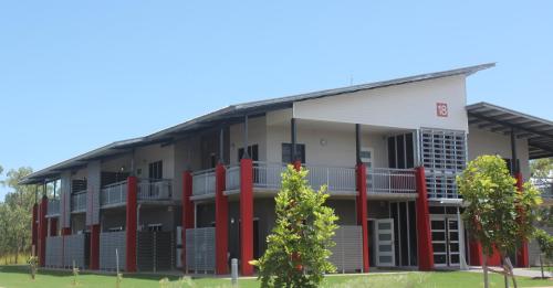 an apartment building with red columns and a tree at CDU Village Casuarina Campus in Jingili