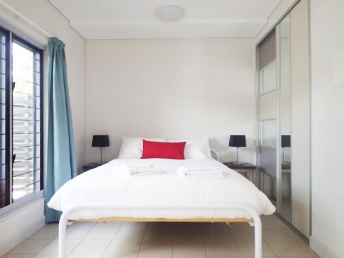 a white bedroom with a white bed with a red pillow at CDU Village Casuarina Campus in Jingili